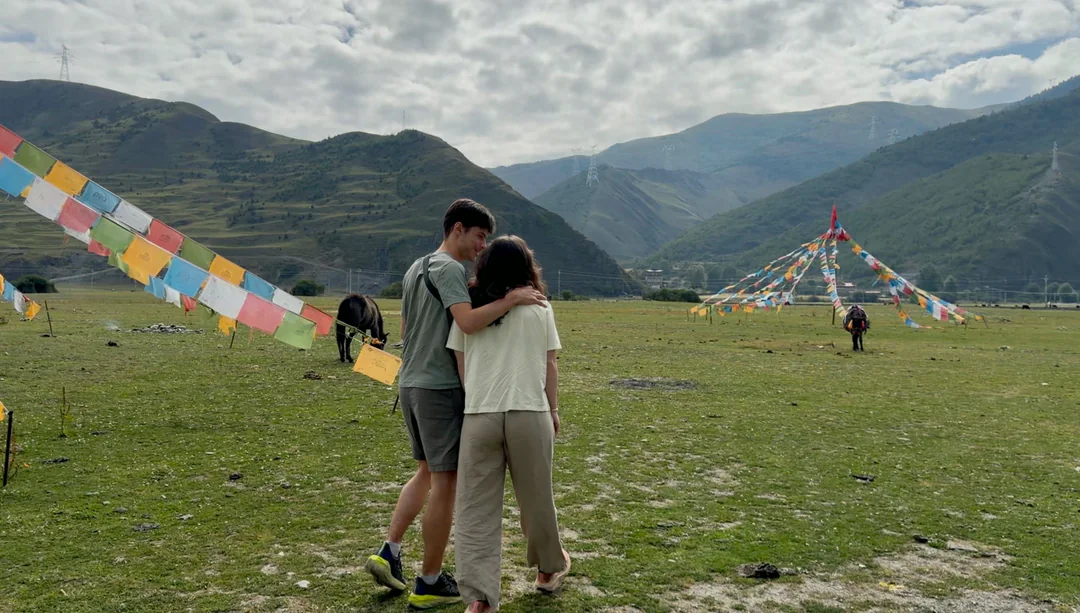 Eva and Martin standing together beneath prayer flags on the grassland